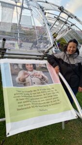 Een foto van Nathalie in het park. Ze zit voor posters met stukken tekst