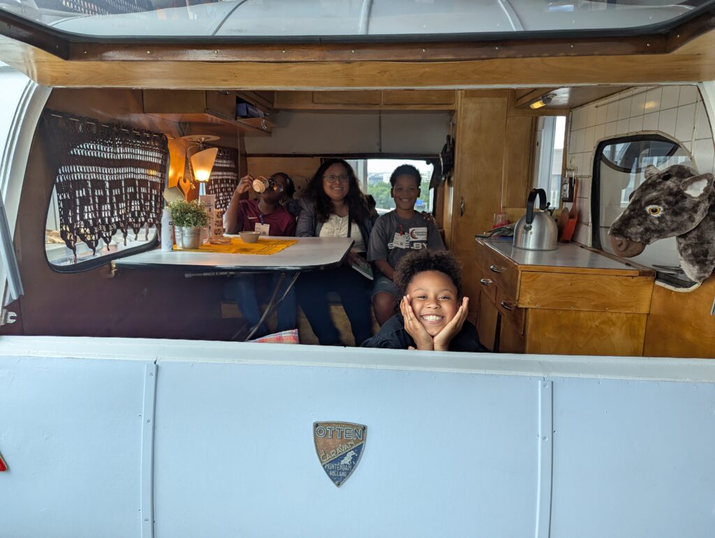 Een foto van drie kinderen die met hun begeleider in een busje zitten