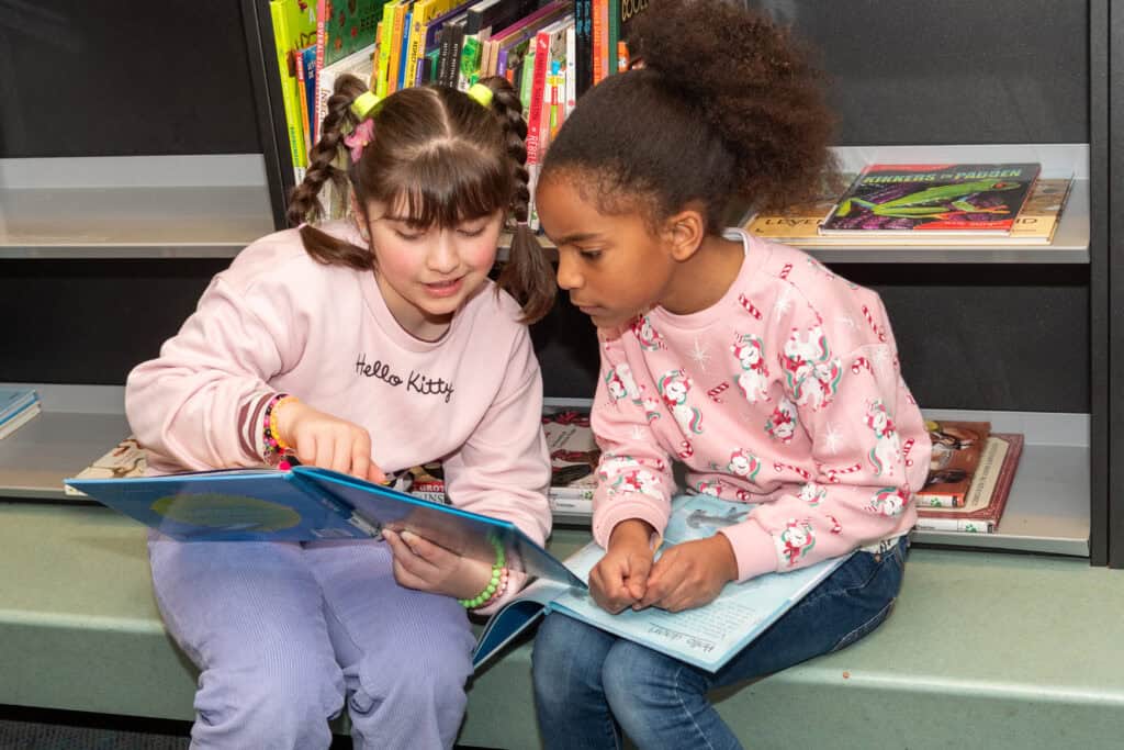 Twee kinderen die ieder met hun eigen boek elkaars boek bespreken